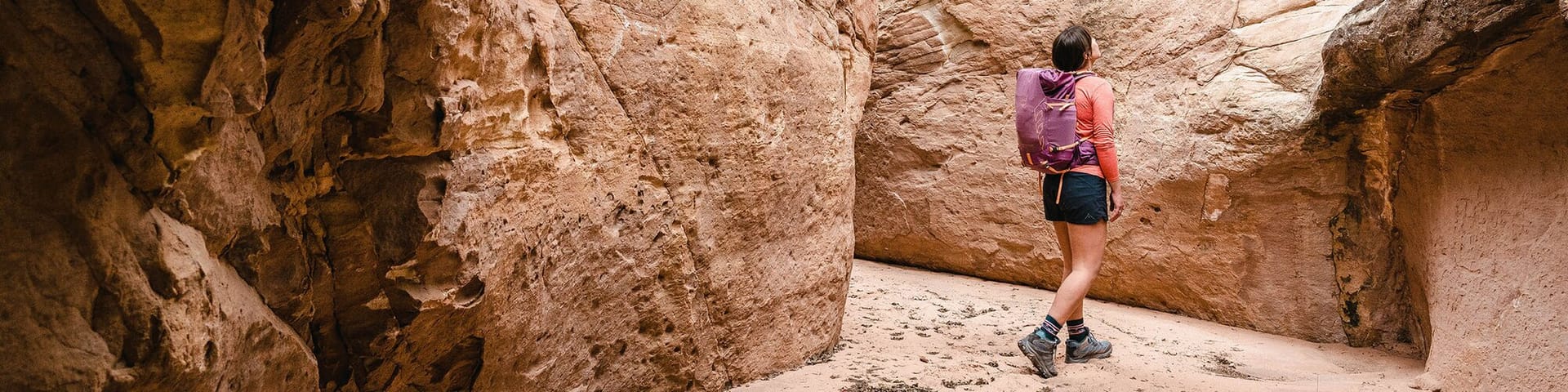 Female day hiker looking up at sandstone wall in slot canyon