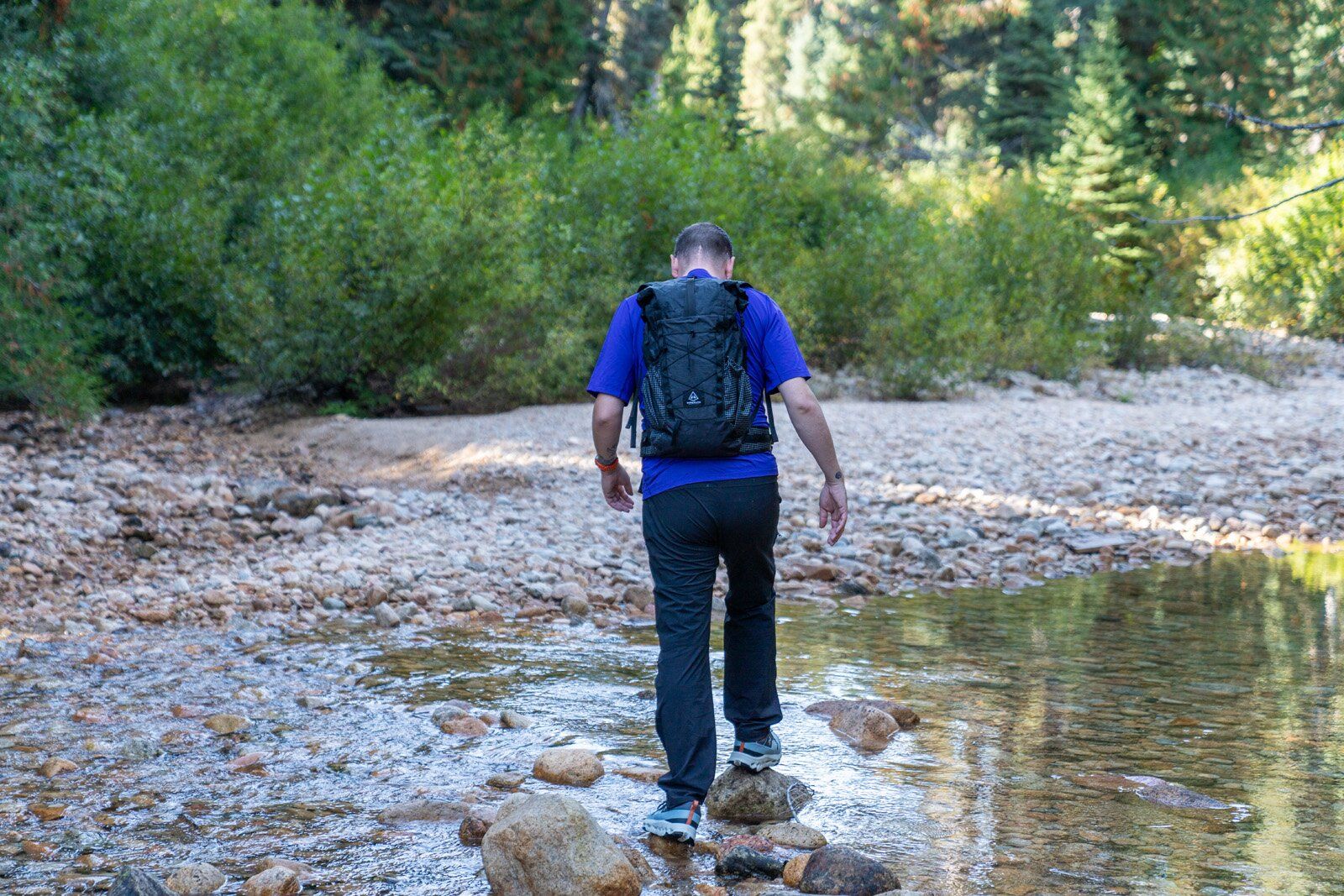 Hiker crossing creek wearing the Hyperlite Mountain Gear Elevate 22 hiking daypack