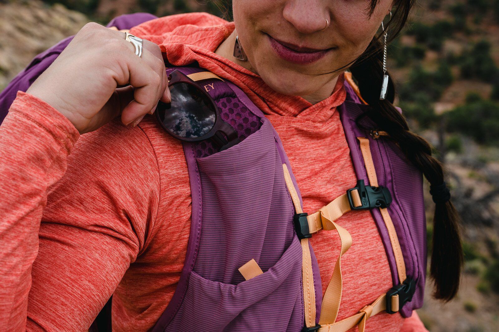 Placing sunglasses into shoulder strap pocket of Osprey Tempest Velocity 30 hiking daypack