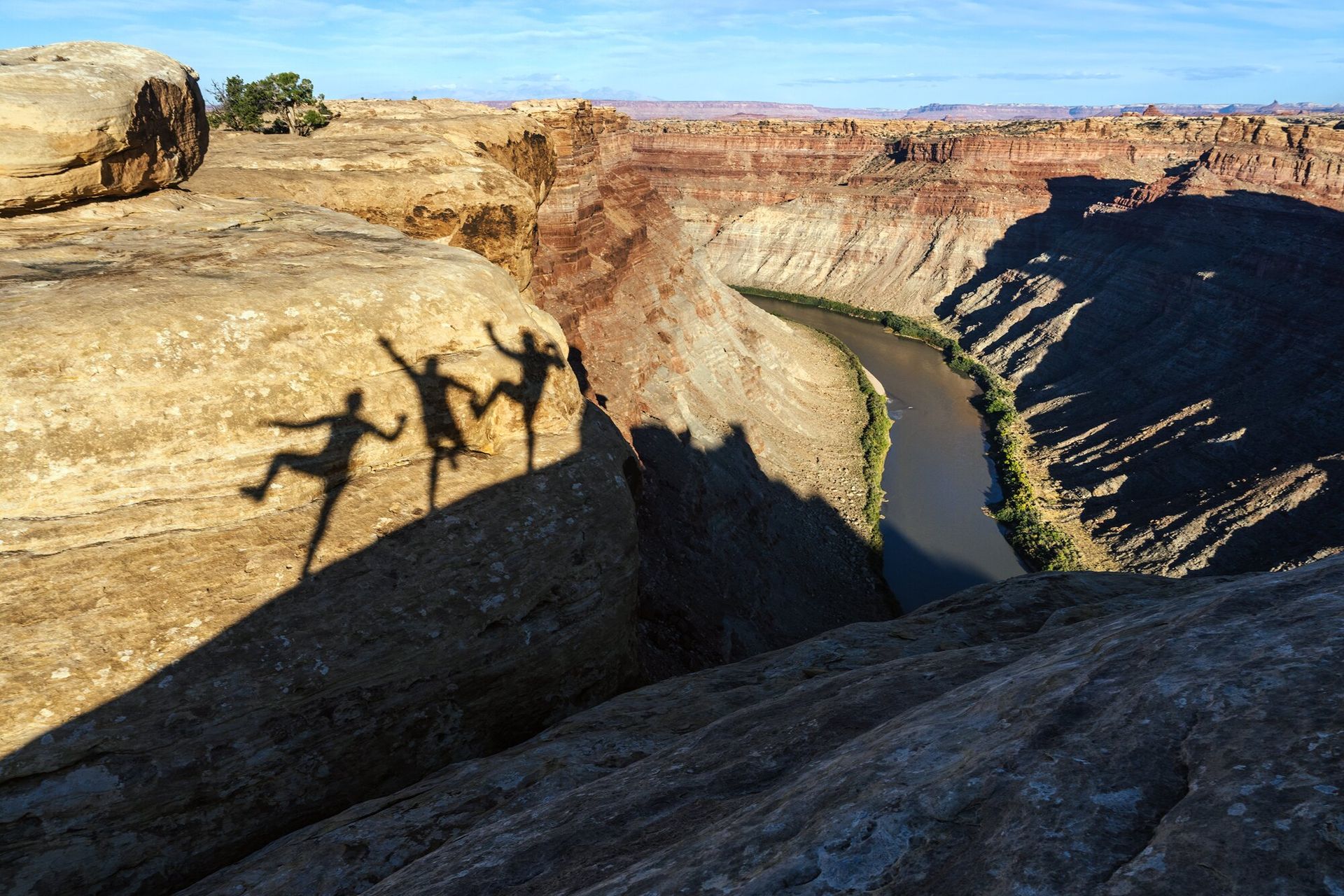 Three human shadows on sandstone wall overlooking deep river canyon