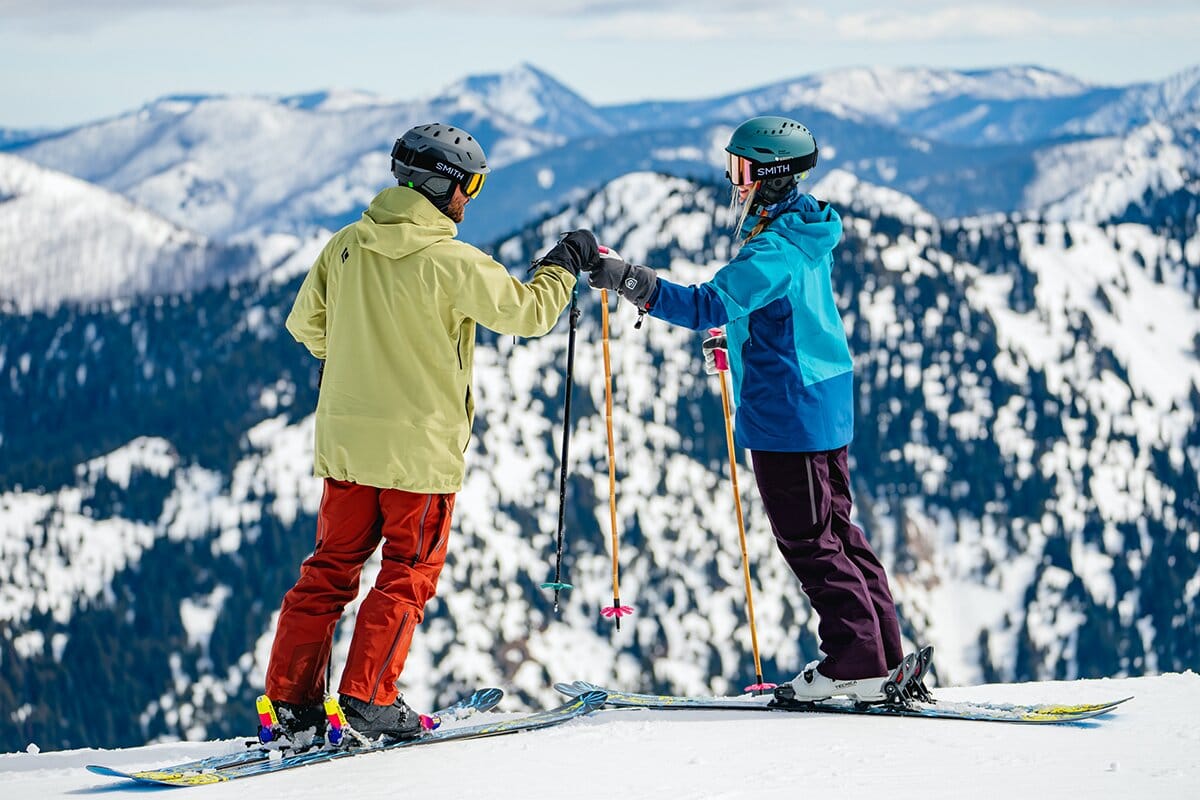 Two skiers fist bumping at top of ski run mobile