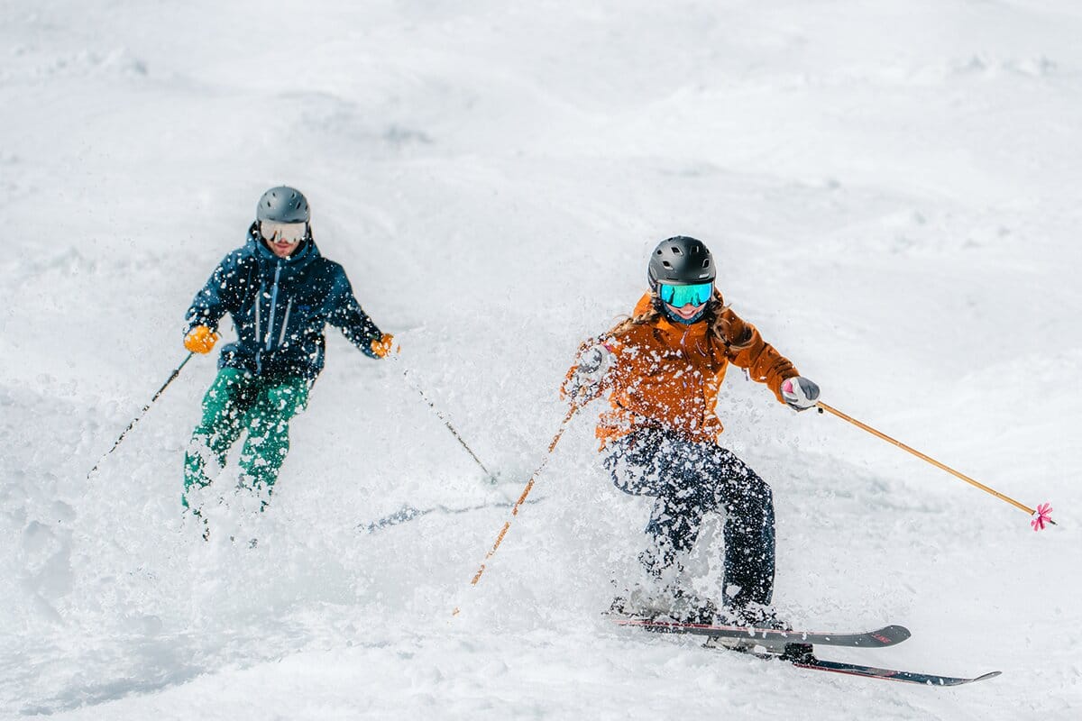 Two skiers skiing corn at the resort wearing ski mittens mobile